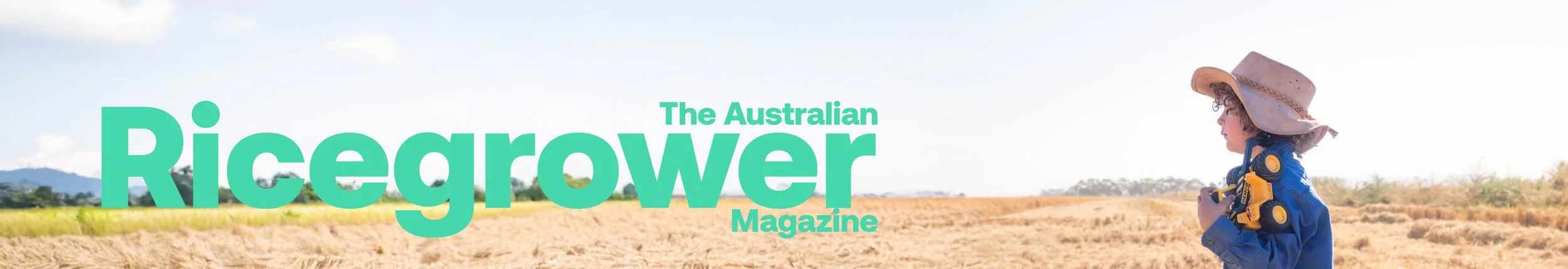 Cover of Australian Ricegrower Magazine featuring a young girl wearing a hat and blue jacket, holding a yellow toy truck, standing in a rice field with blue sky and distant hills.