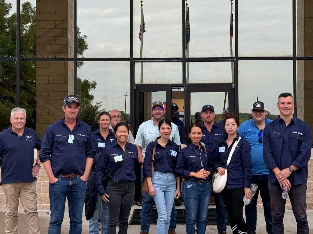 Group of people standing outside in front of a building with glass windows and flags, some holding water bottles, posing for a photo.
