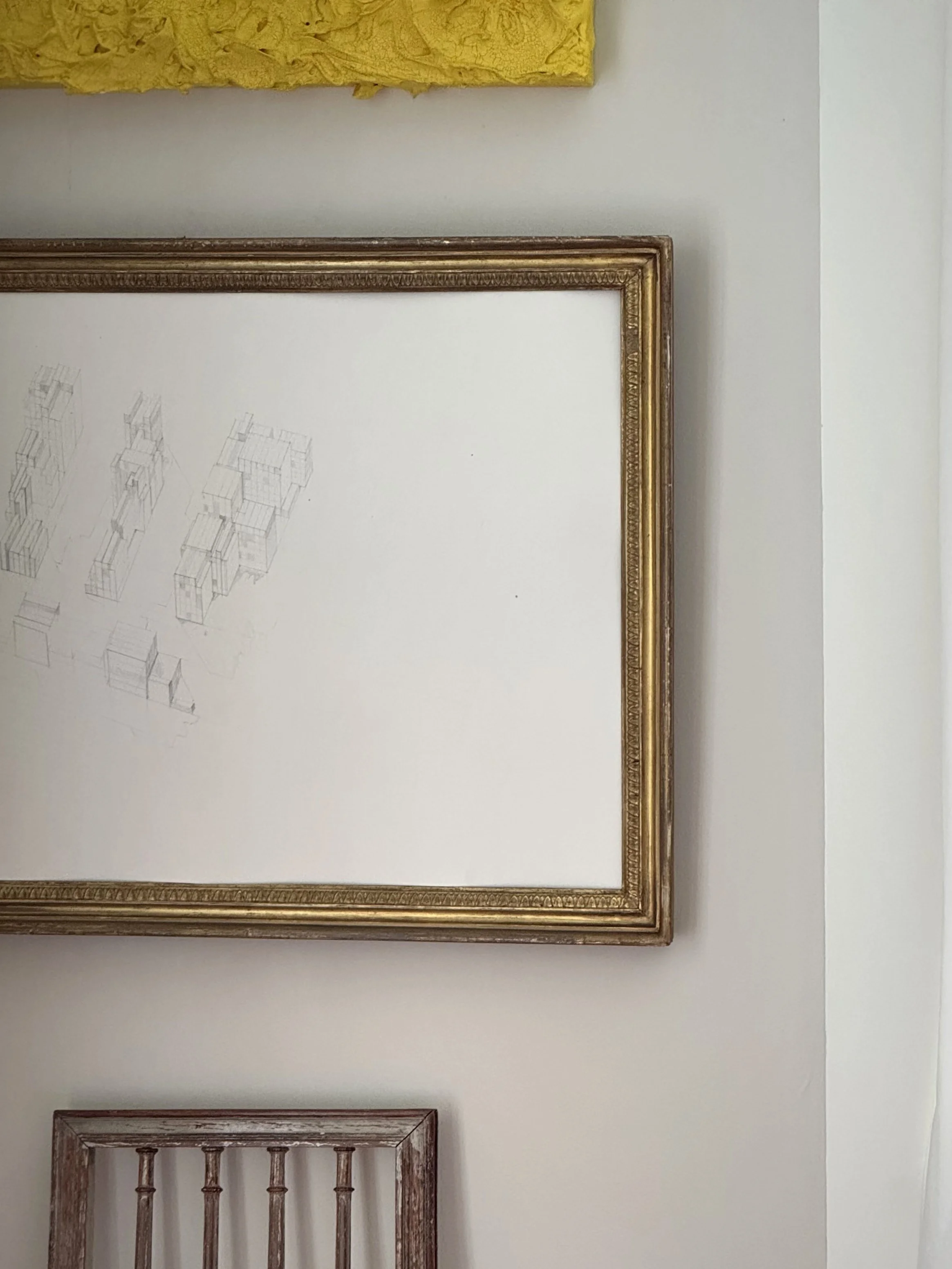 Part of an art gallery wall shows a framed piece with architectural sketches and a yellow textured artwork above it.