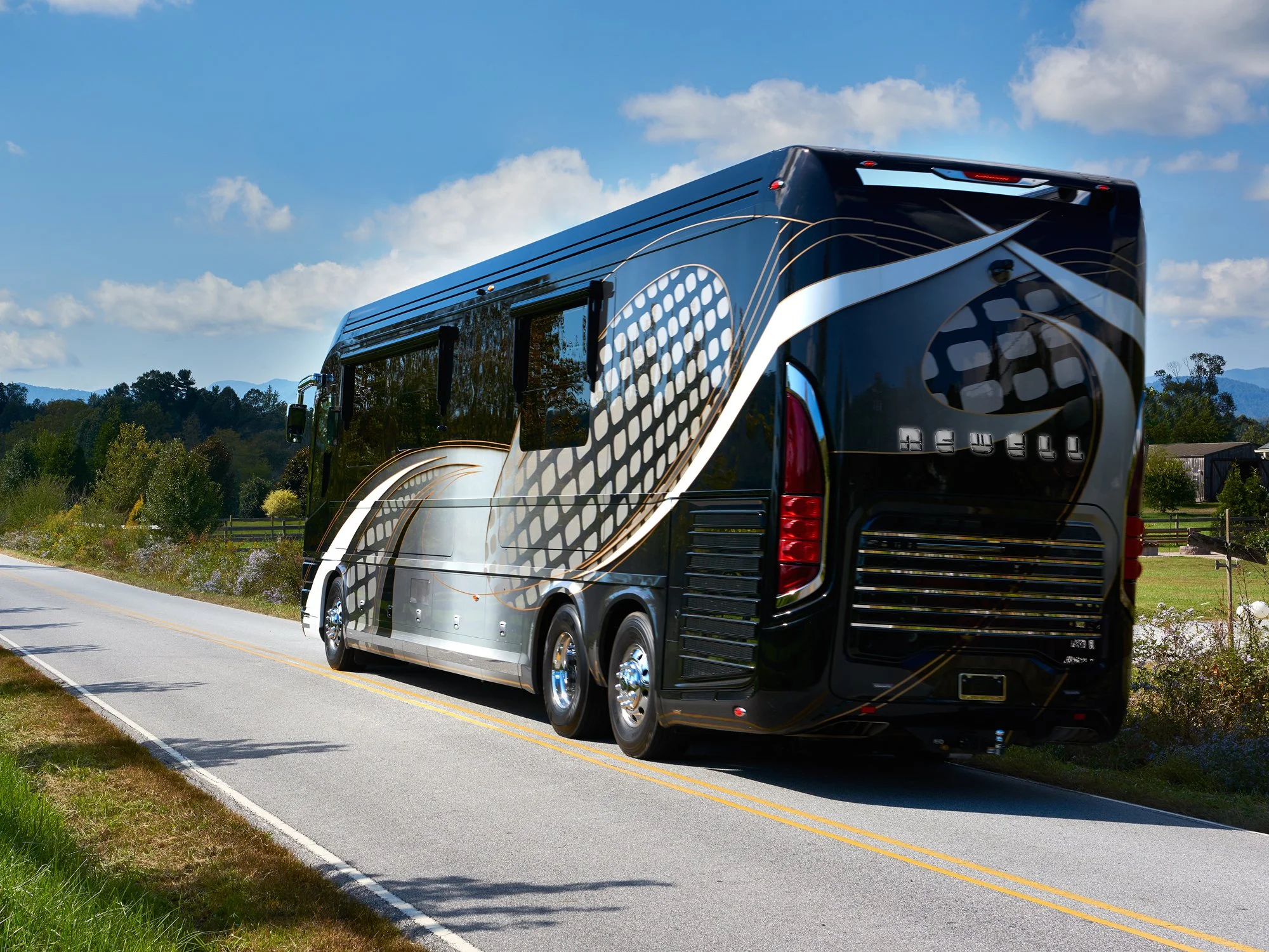 Rear view of a black Newell Coach luxury motorhome driving on a scenic road.