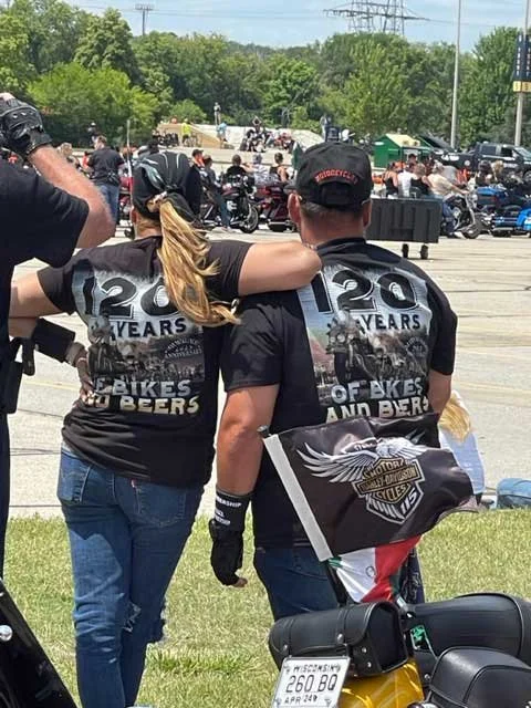 Two people from behind, wearing matching black t-shirts that say "120 YEARS OF BIKES AND BEERS".
