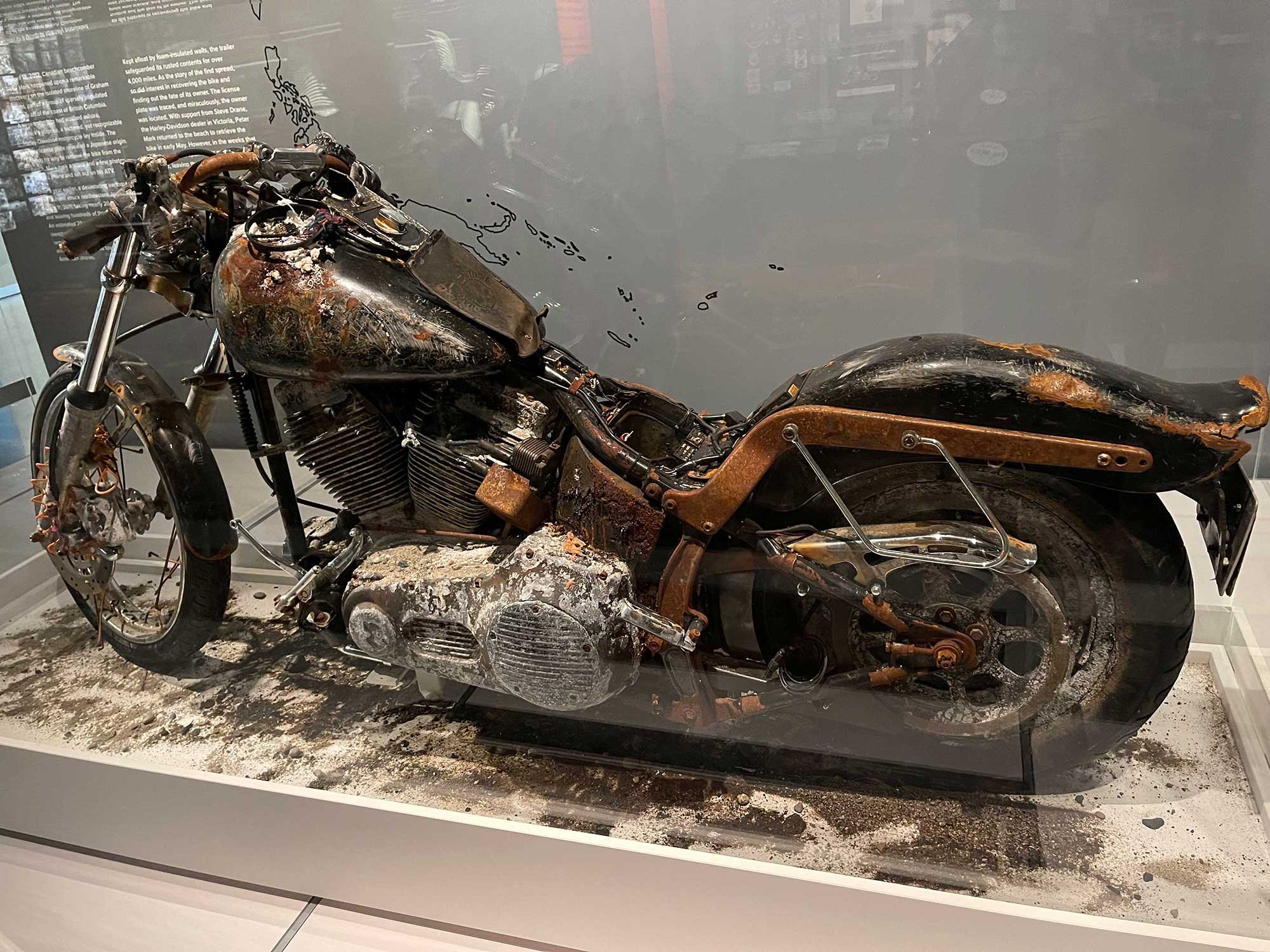 A heavily rusted and damaged motorcycle is displayed in a museum exhibit.