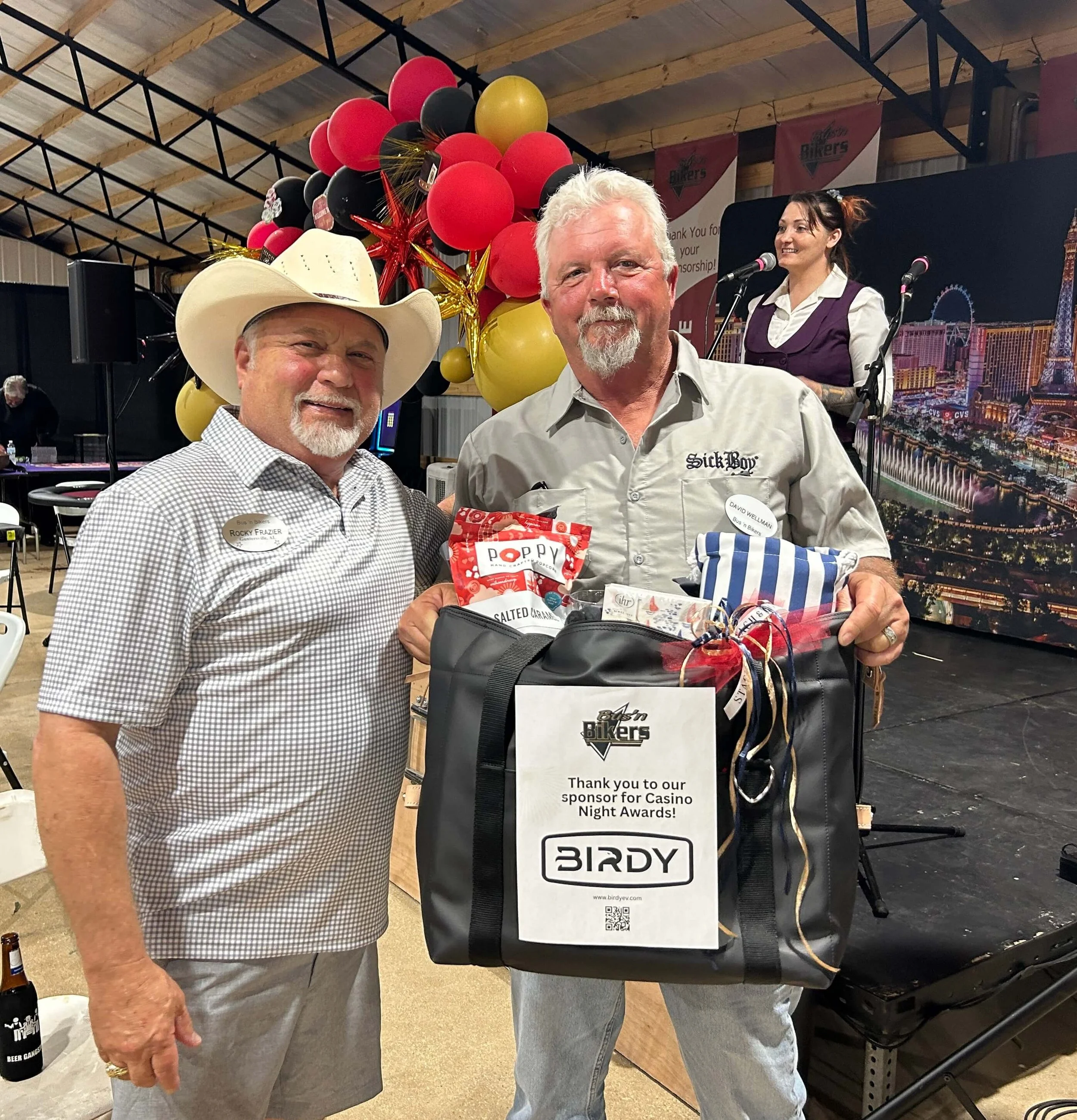 Rocky F. and David W. holding gifts and smiling after a successful casino night, with balloons in the background