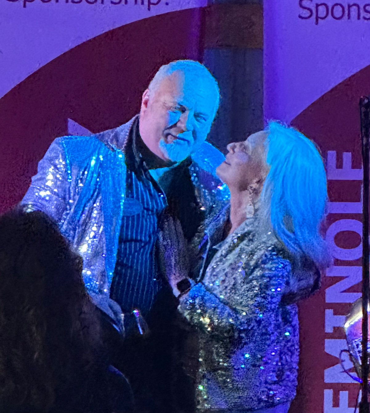 Pamela and Rocky Fraizer sharing a moment, both wearing sparkling outfits at a rally event.