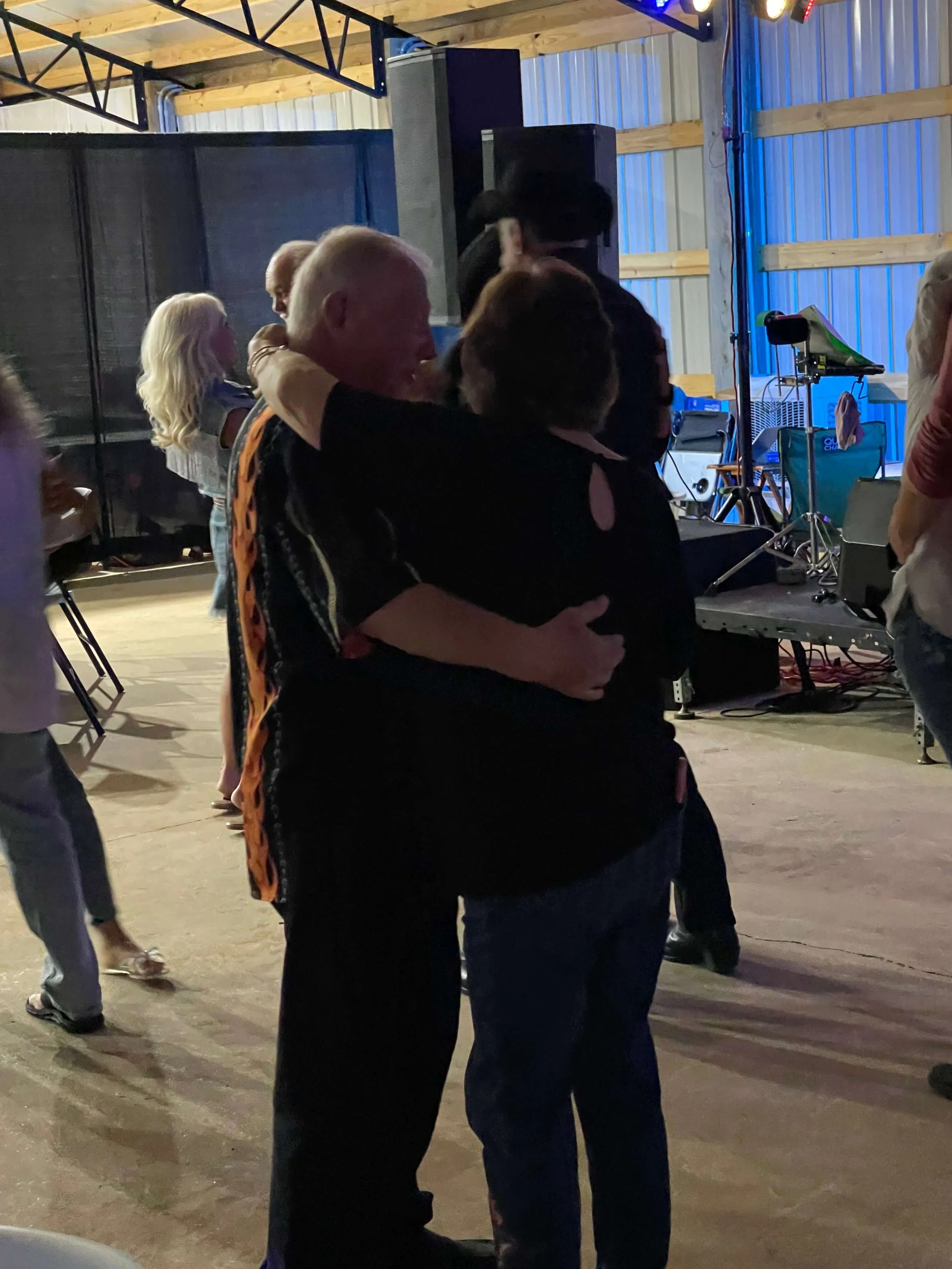 A couple sharing a slow dance in a dimly lit barn venue with live music in the background.