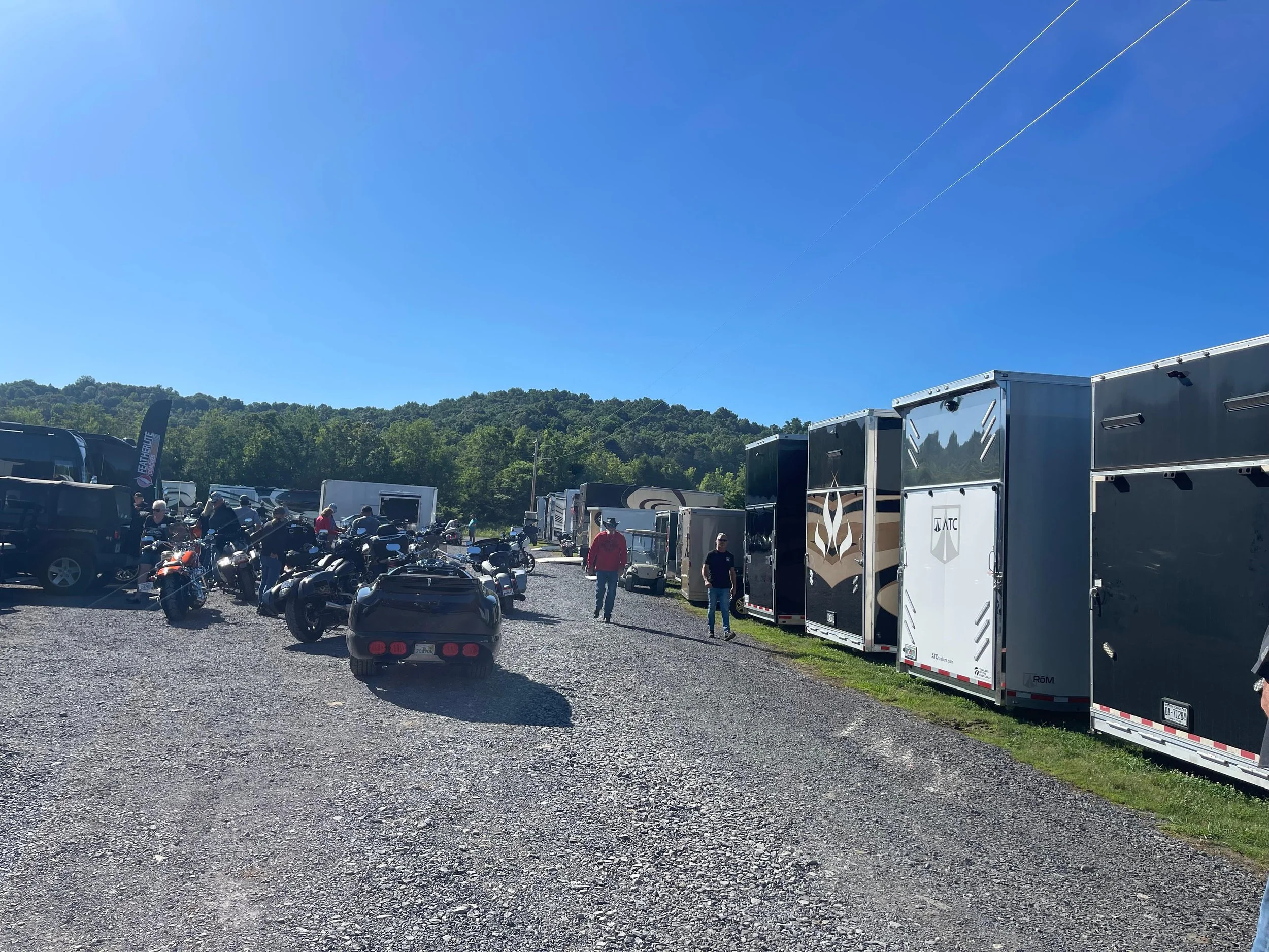 Motorcycles parked alongside trailers under a clear sky at a biker rally event.
