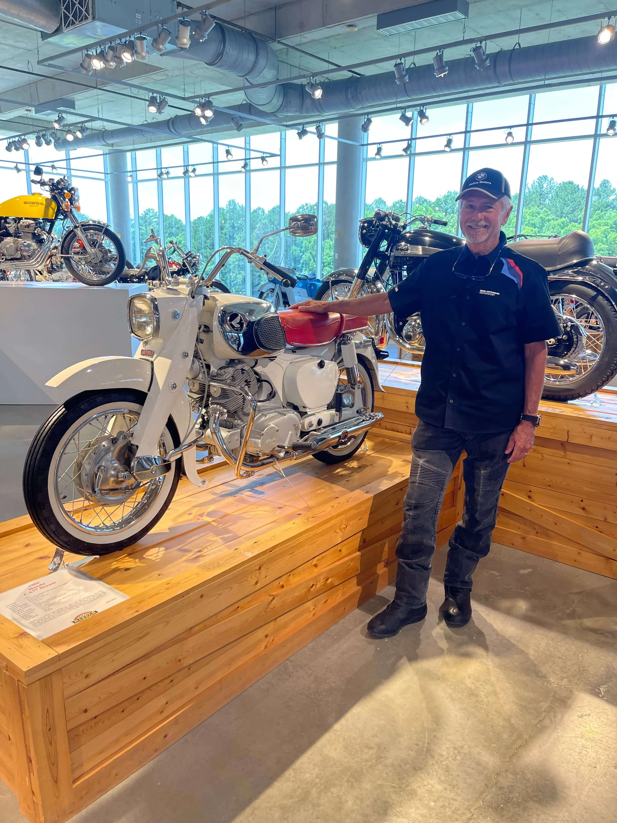 Phil Meaux standing next to a classic motorcycle in a museum display.