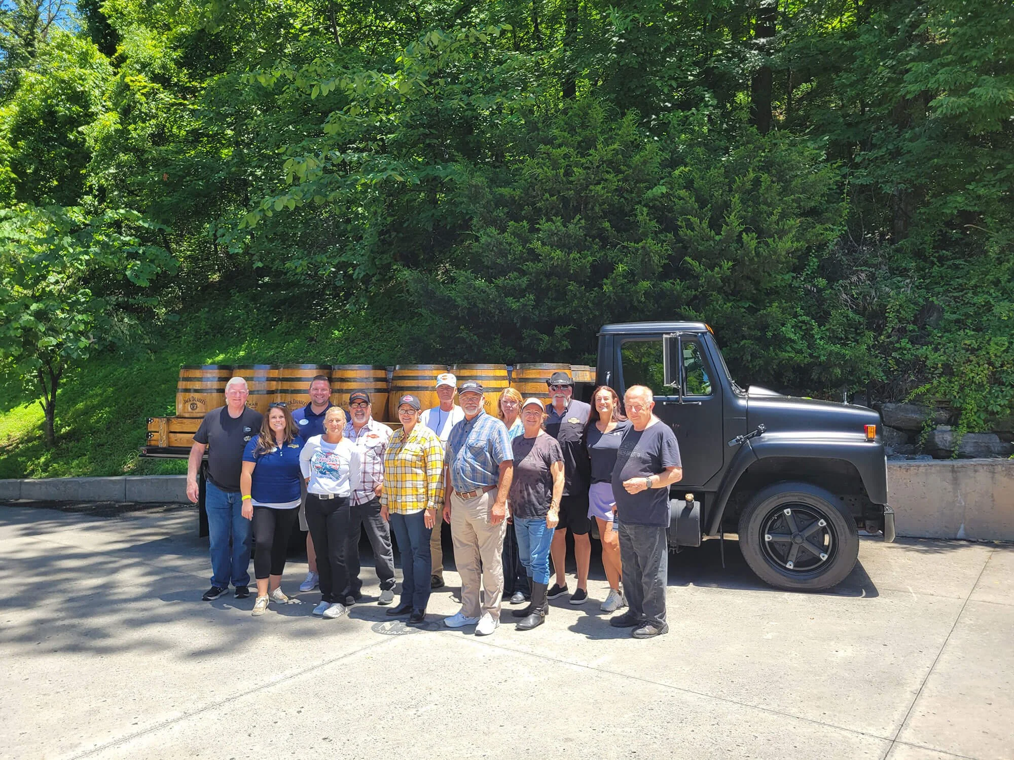 A Bus ’n Bikers group posing in front of a black truck at the Jack Daniel's distillery, surrounded by barrels at Jack Daniels.