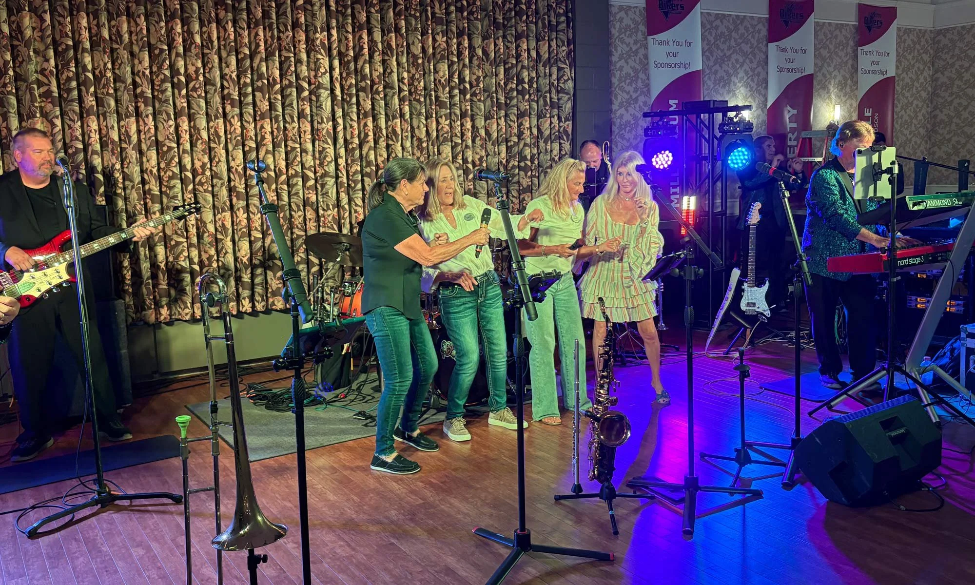A live band performing on a stage, featuring four women singing in the center