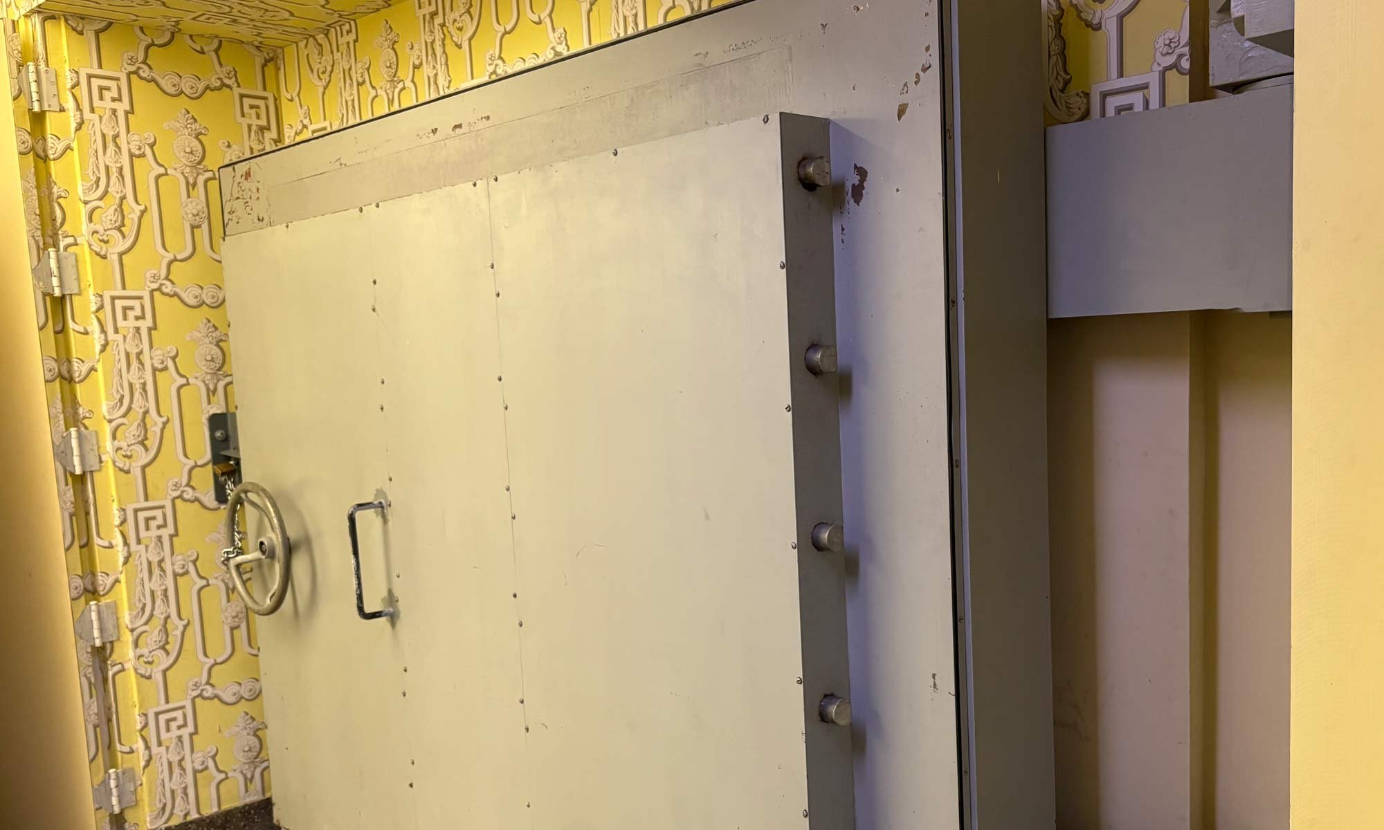 A massive, grey bank vault door set against bright yellow patterned wallpaper.