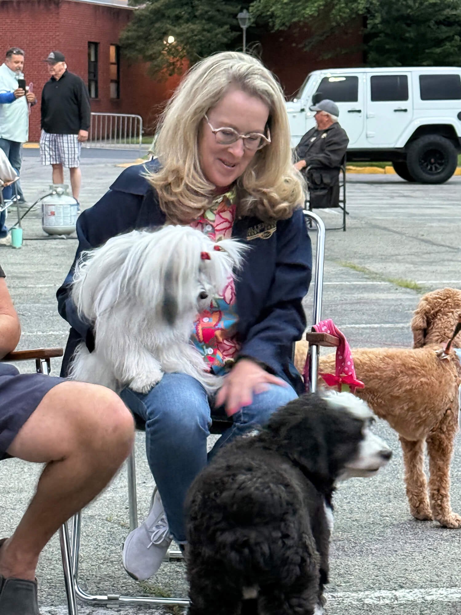 A woman sitting and petting a small white dog, with other dogs nearby.