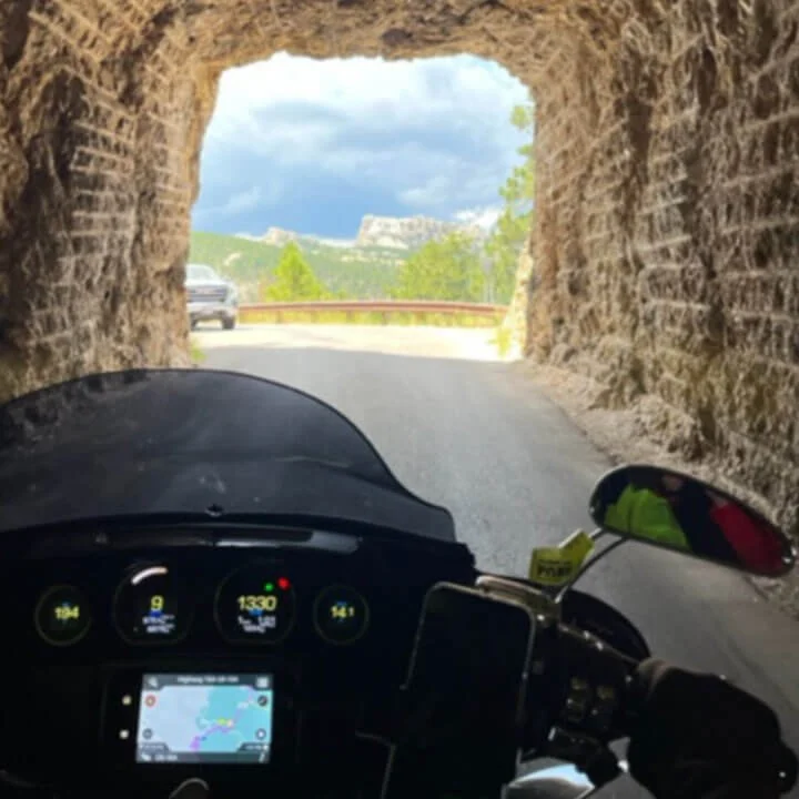 Rider's view from motorcycle driving through a stone tunnel.