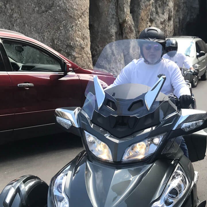 Rider on a gray three-wheeled motorcycle driving through a narrow rock passage.