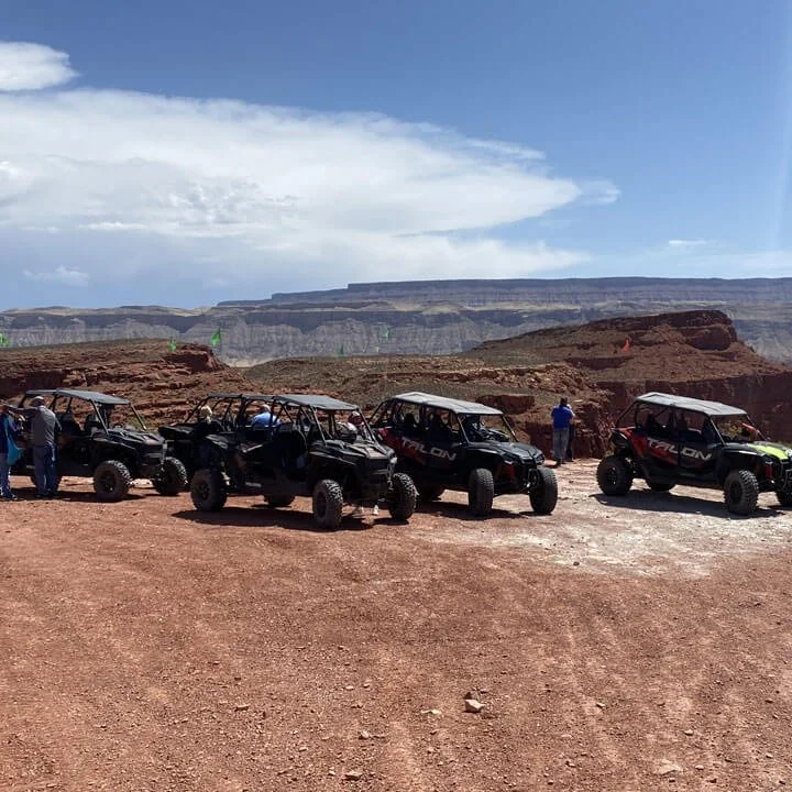 Group of off-road UTVs lined up on red rock terrain with canyon landscape in background during desert tour.