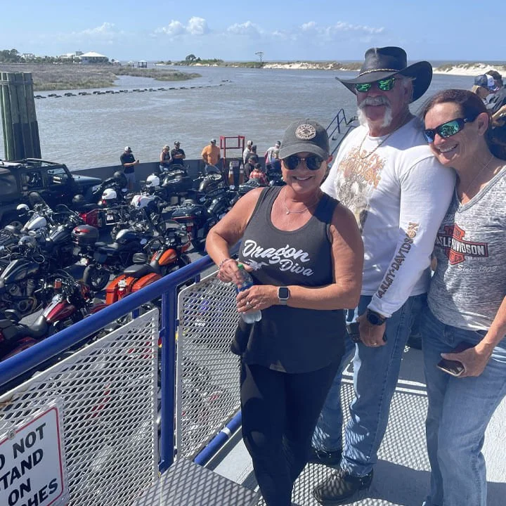 Three friends on ferry deck with motorcycles loaded below during a ferry crossing.