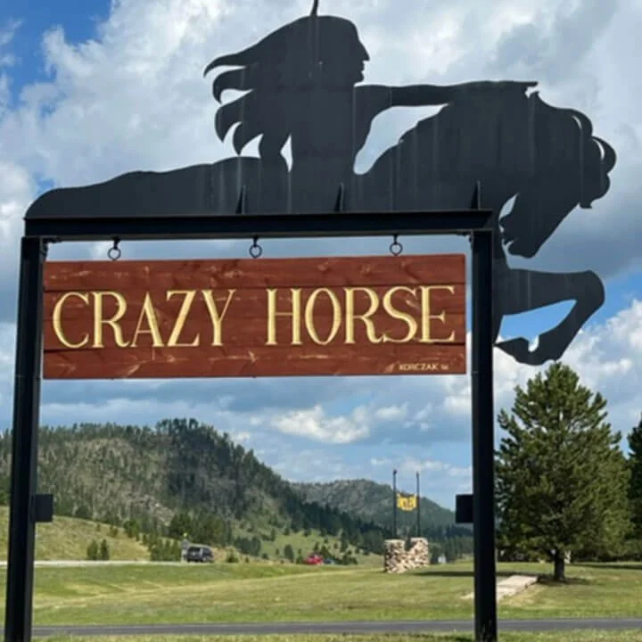 Crazy Horse Memorial entrance sign with metal horse silhouette against mountain backdrop in South Dakota.
