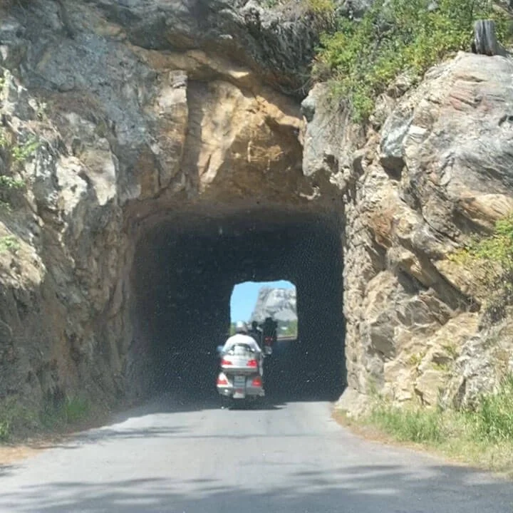 Bus'n Bikers motorcycle rider approaching historic stone tunnel on scenic mountain road adventure.
