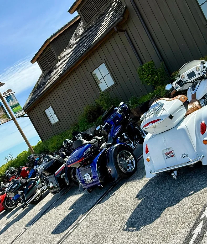 Line of touring motorcycles and trikes parked outside a rustic wood building at Top of the Rock Heritage Preserve.