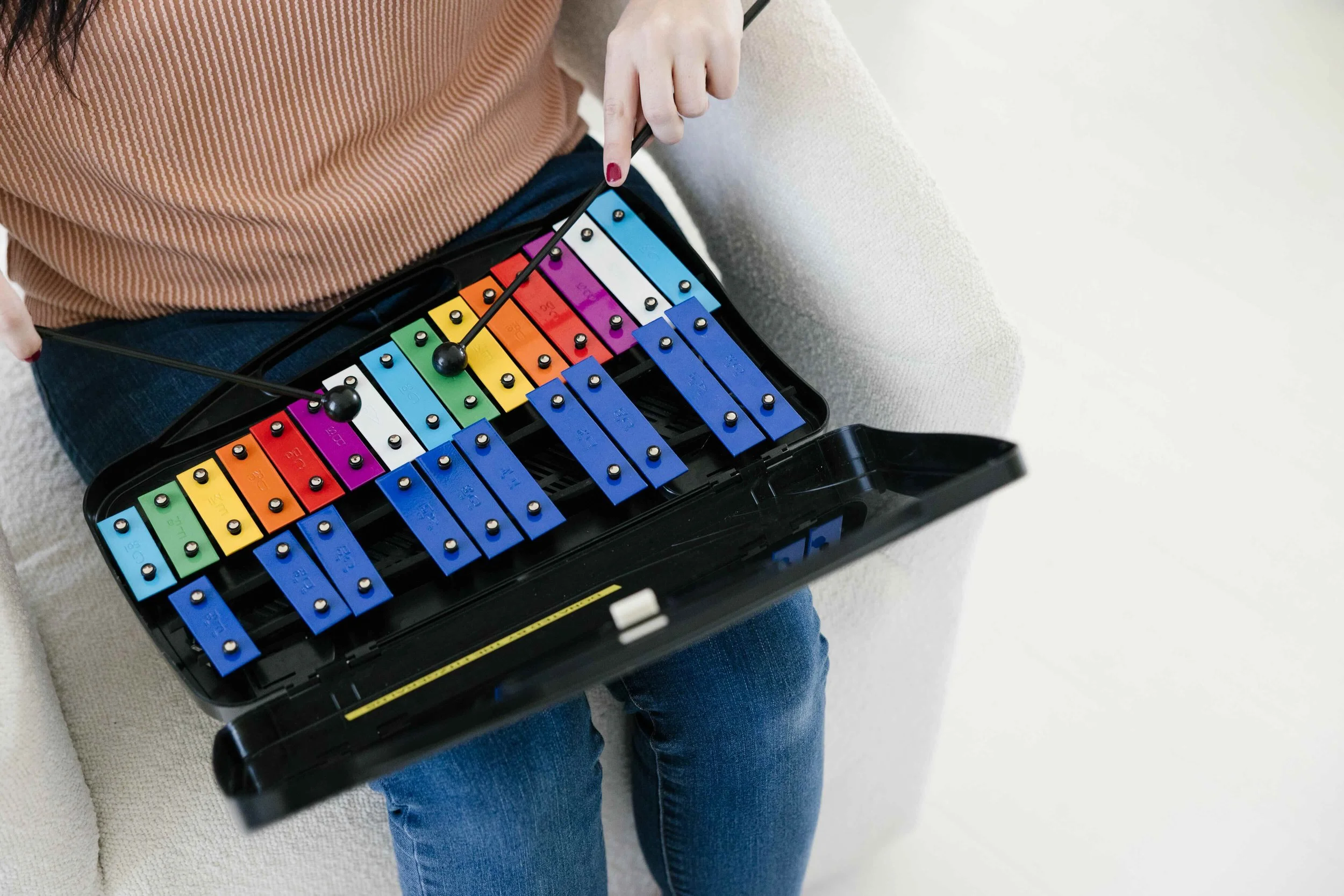 Person sitting on a couch playing a colorful xylophone with rainbow-colored xylophone.