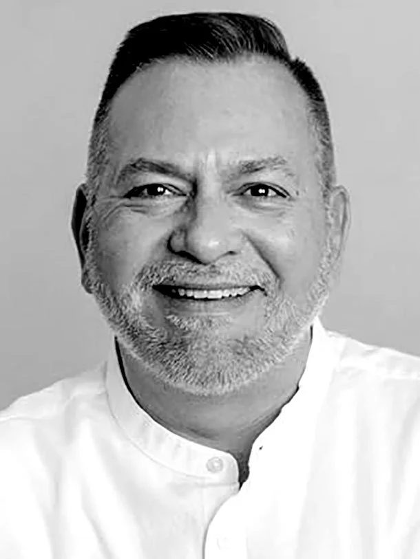 Black and white photograph of a smiling man with short dark hair and a beard, wearing a white shirt with a Mandarin collar.