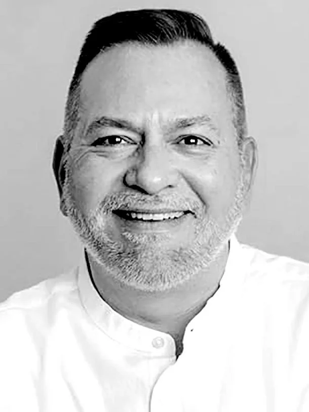 A smiling middle-aged man with short dark hair, a beard, and mustache, wearing a white collared shirt.