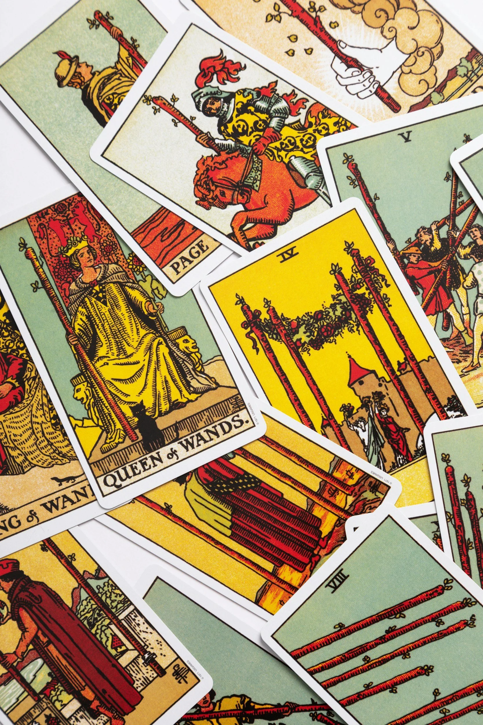 A spread of Tarot cards, including the Queen of Wands, the Page of Swords, and the Five of Wands, arranged overlapping on a surface.