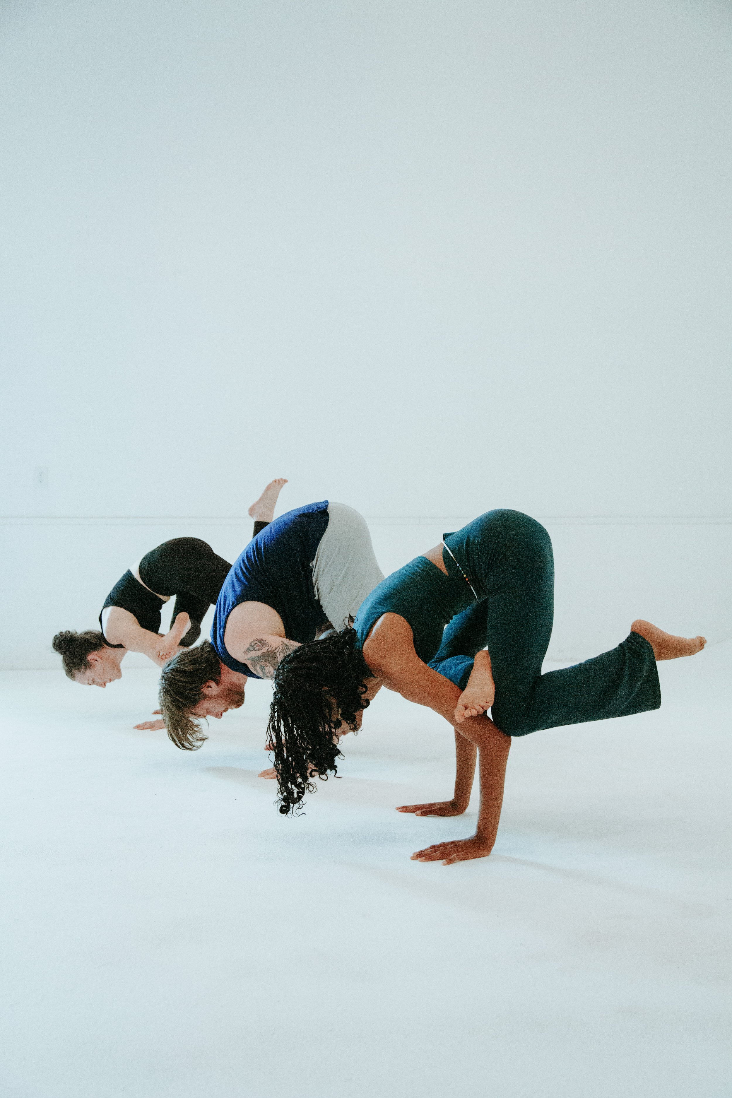 People practicing yoga in a studio, balancing on their hands with their legs bent or extended, over a white background.