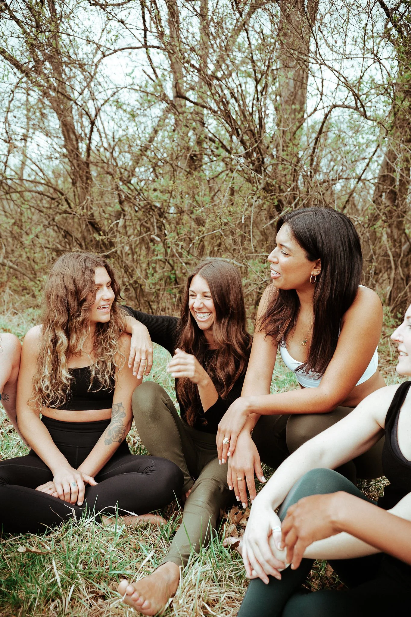 Group of women sitting on the grass and laughing in a wooded area.