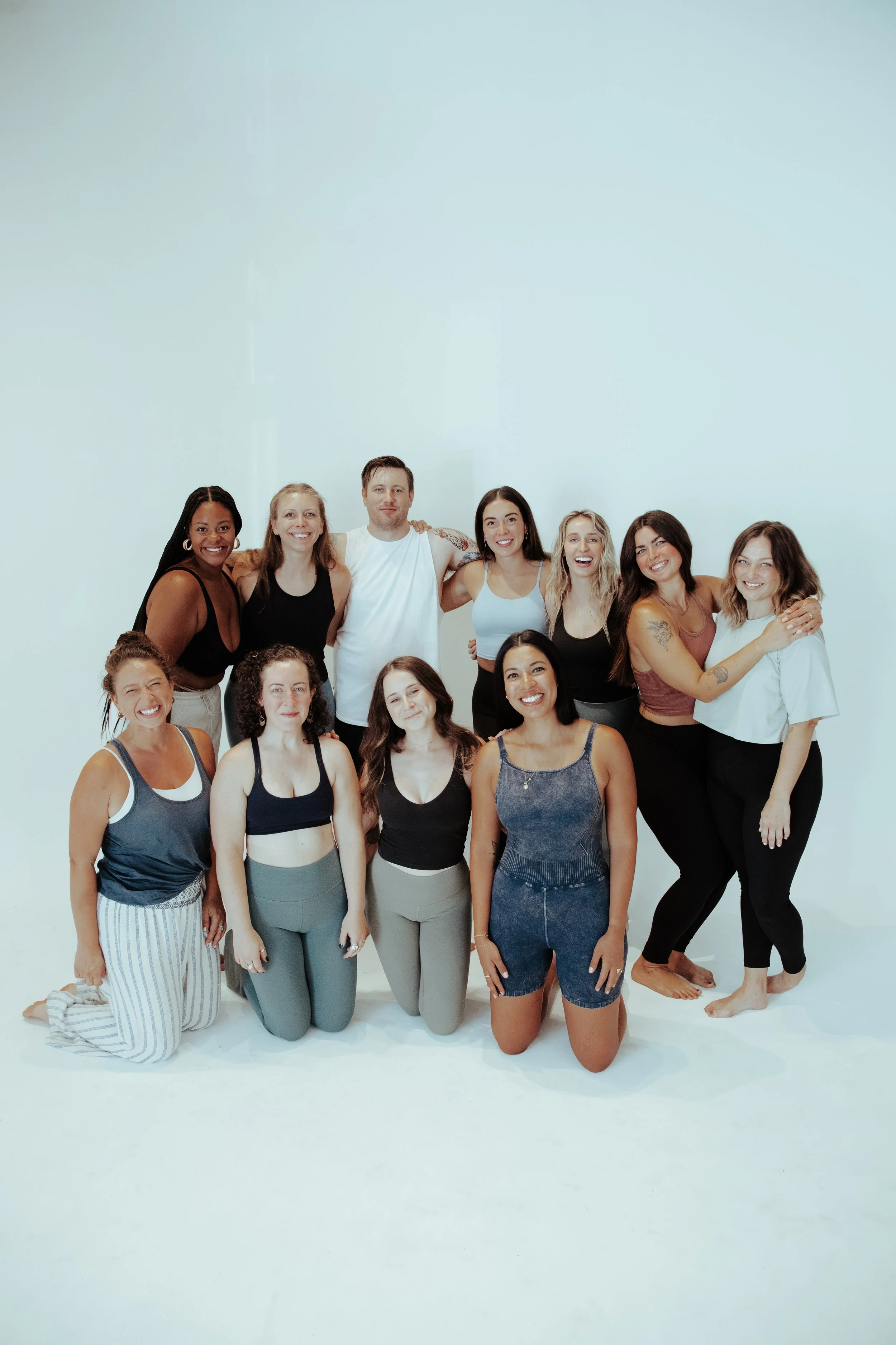 Group of ten diverse women and one man, smiling, in casual sportswear, posing in a white studio.
