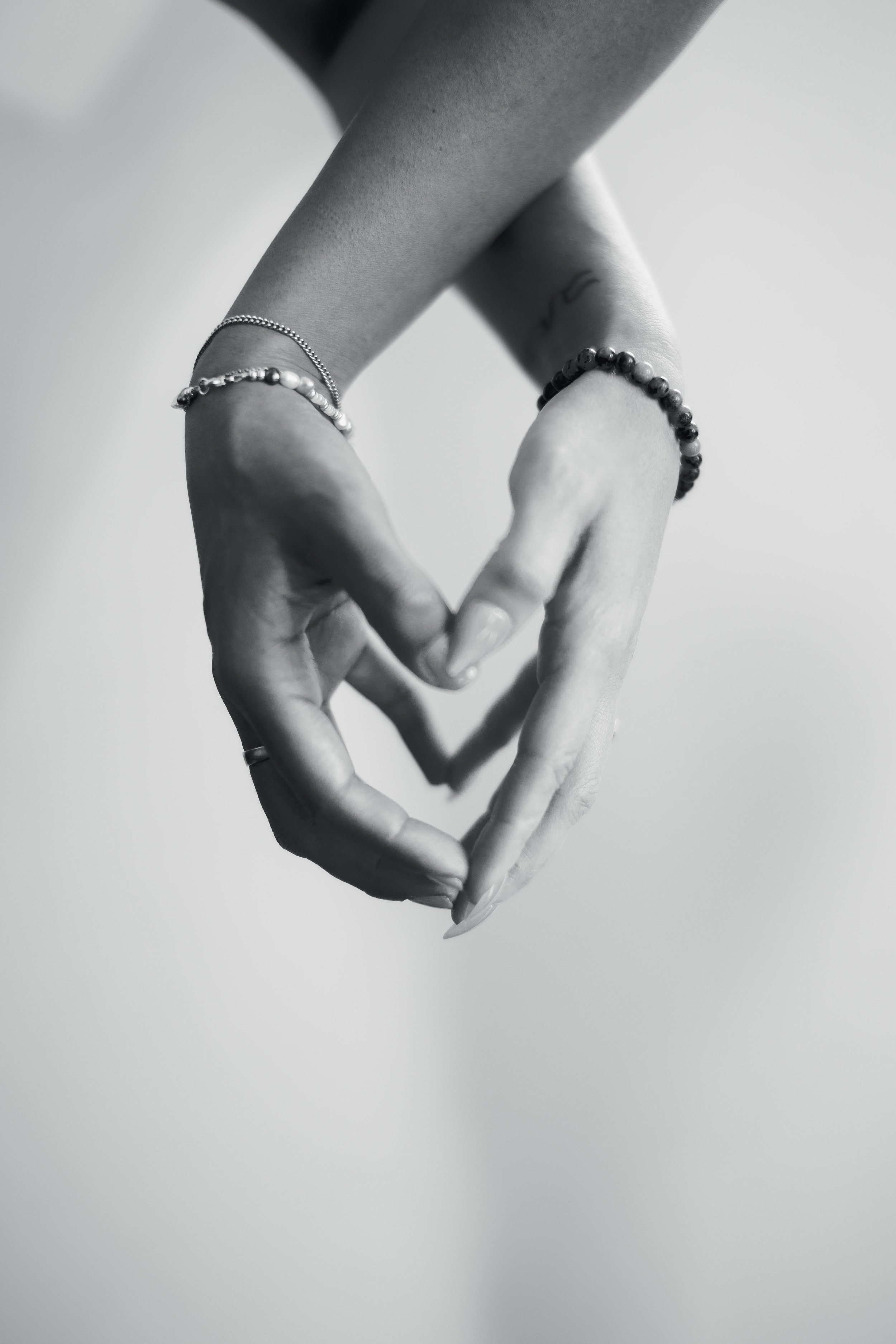 Close-up of two hands forming a heart shape, one with jewelry, in black and white.