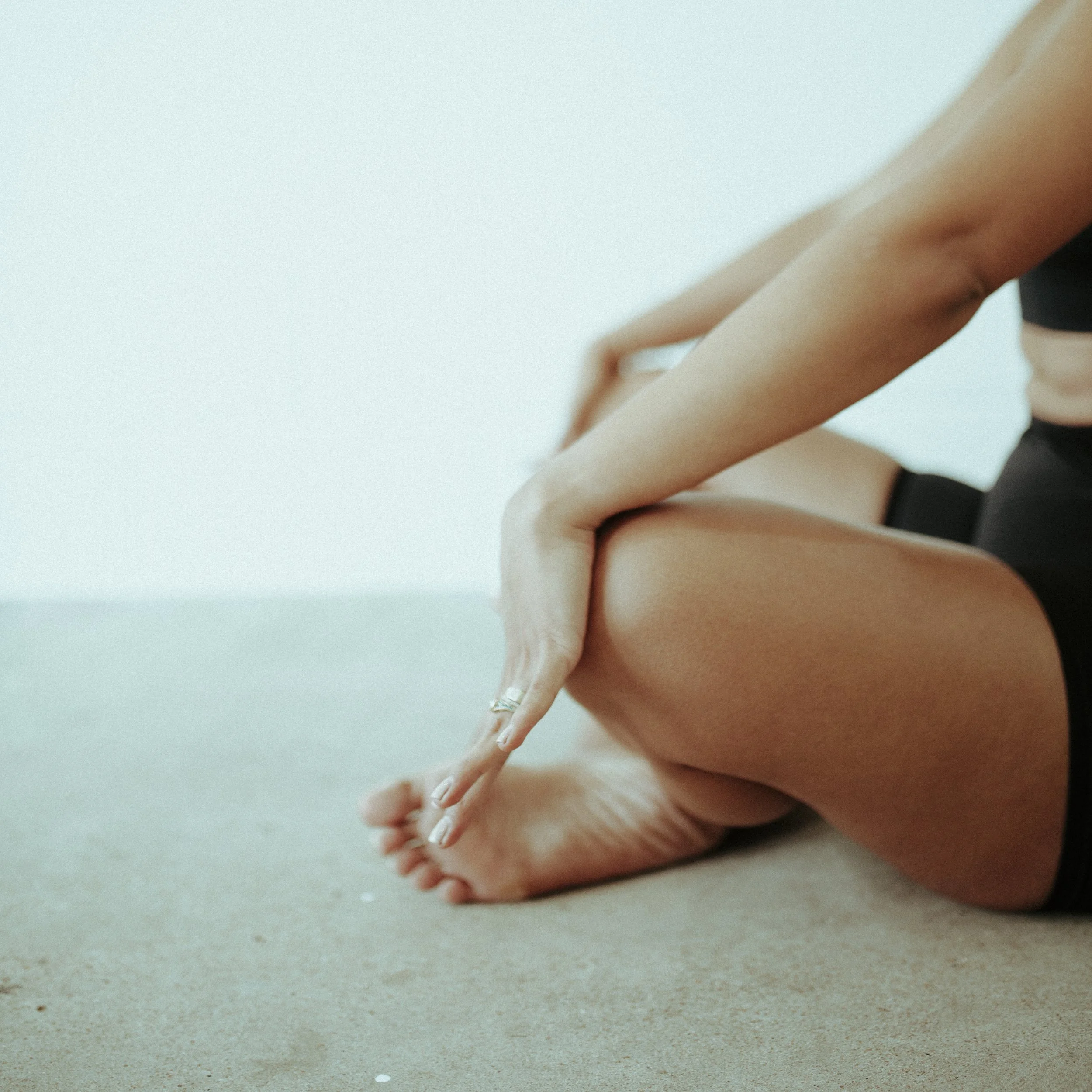 A person stretching or exercising on a beige carpeted floor, with one foot flat on the ground and the other leg bent, hands reaching toward the foot.