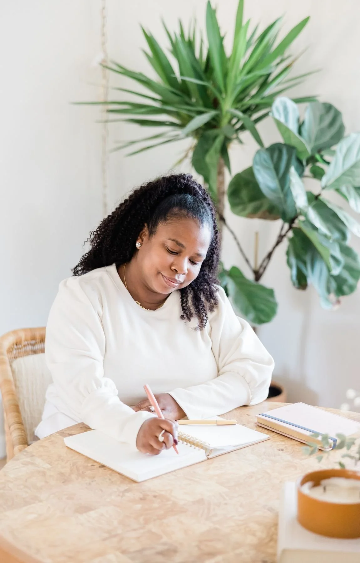 A woman attends a journaling workshop, writing in her notebook, surrounded by plants and stationery in a bright, cozy room in Minneapolis, Minnesota