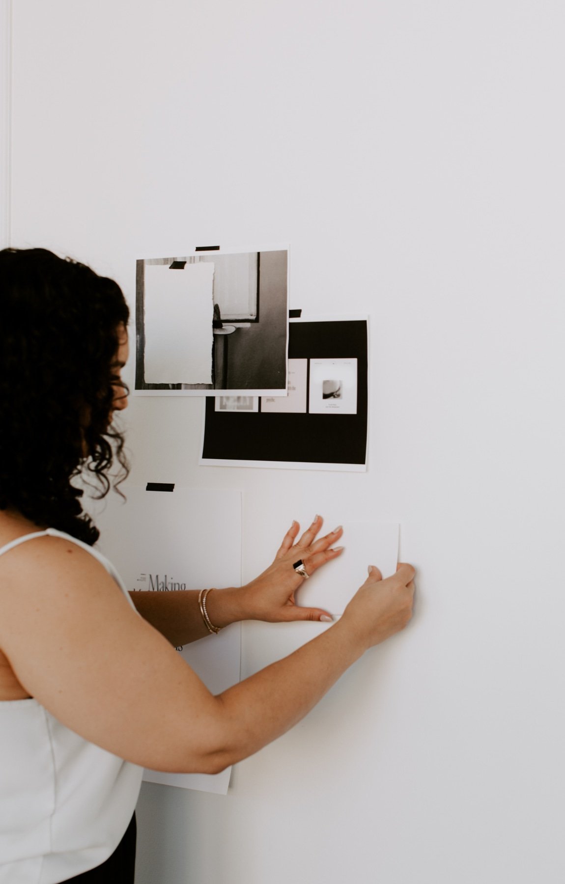 A person with curly hair teaches a vision board workshop, attaching papers and photos to a white wall in Minneapolis Minnesota