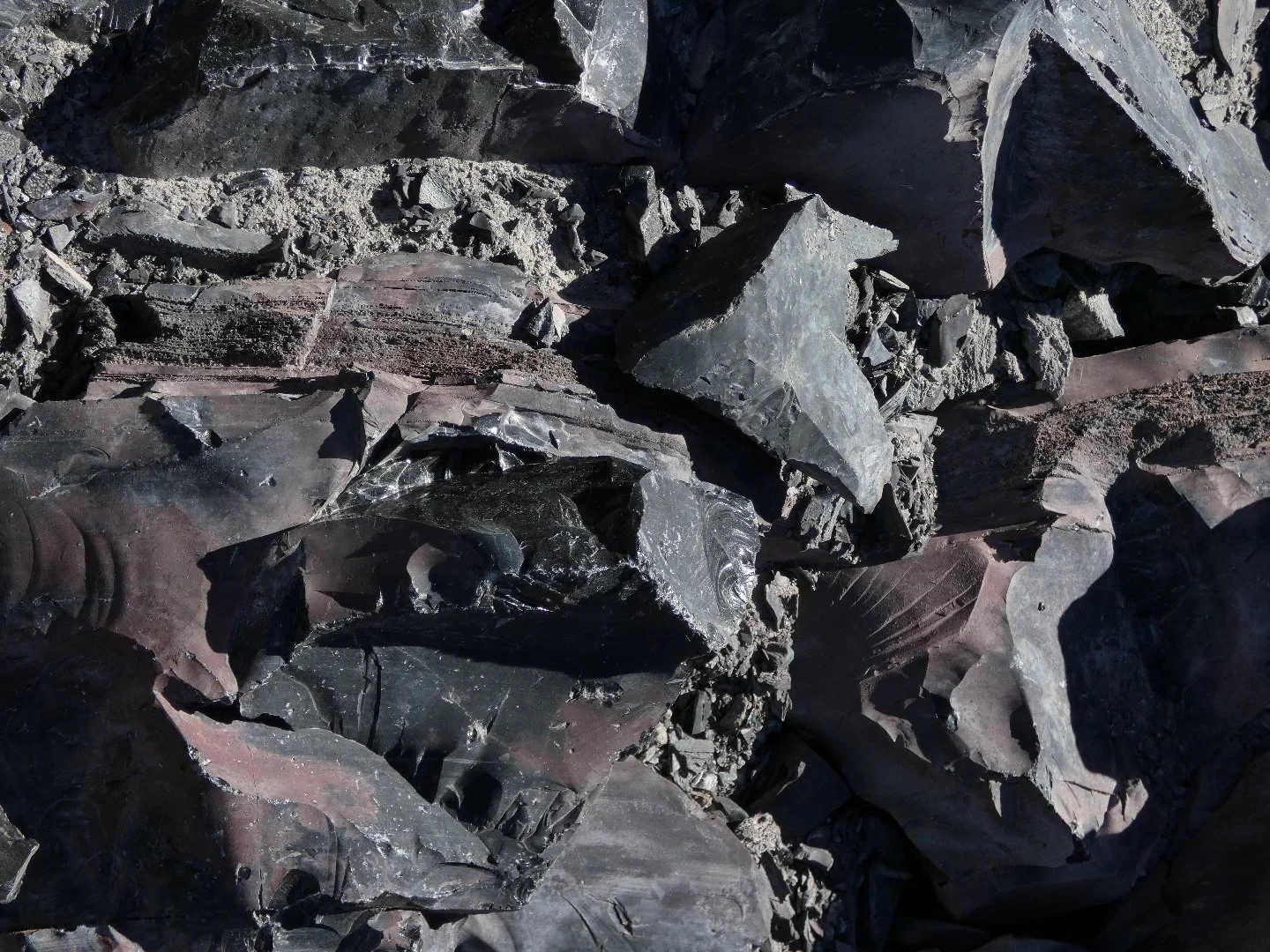 Close-up of dark gray and black shattered rocks and mineral fragments on the ground.