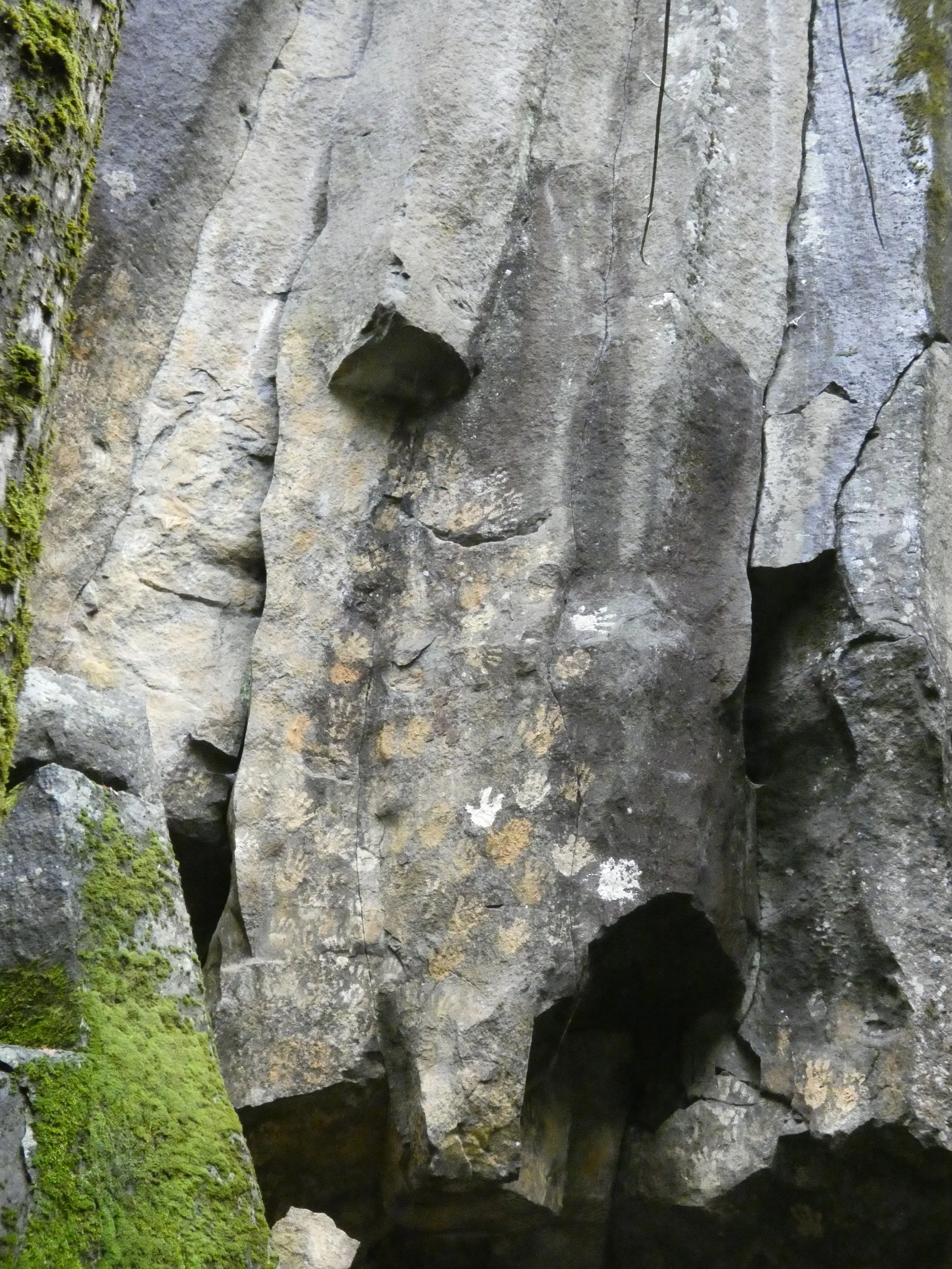 Close-up of a rock face with small crevices, some moss on the left side, and two ropes hanging down, indicating a climbing or spelunking area.