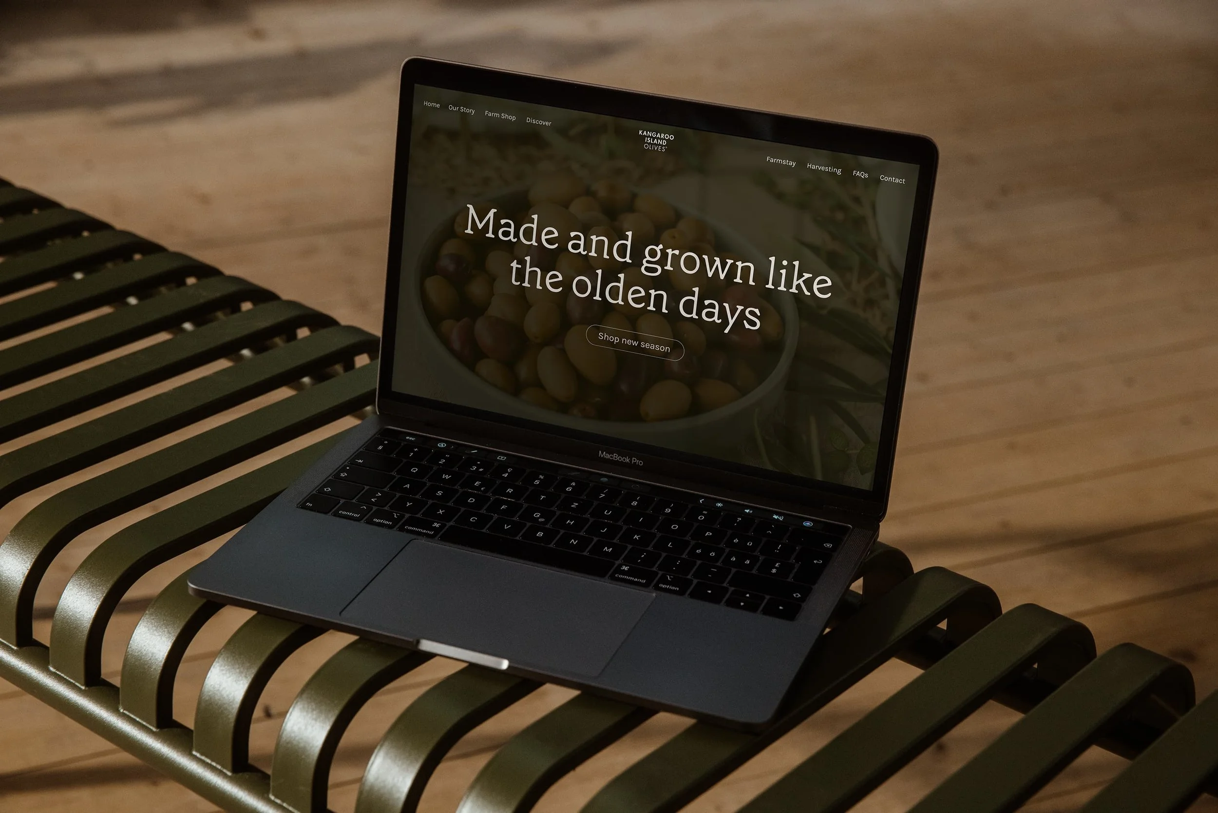 A MacBook Pro laptop displaying a website with the text 'Made and grown like the olden days' on a bench with black and green slats.