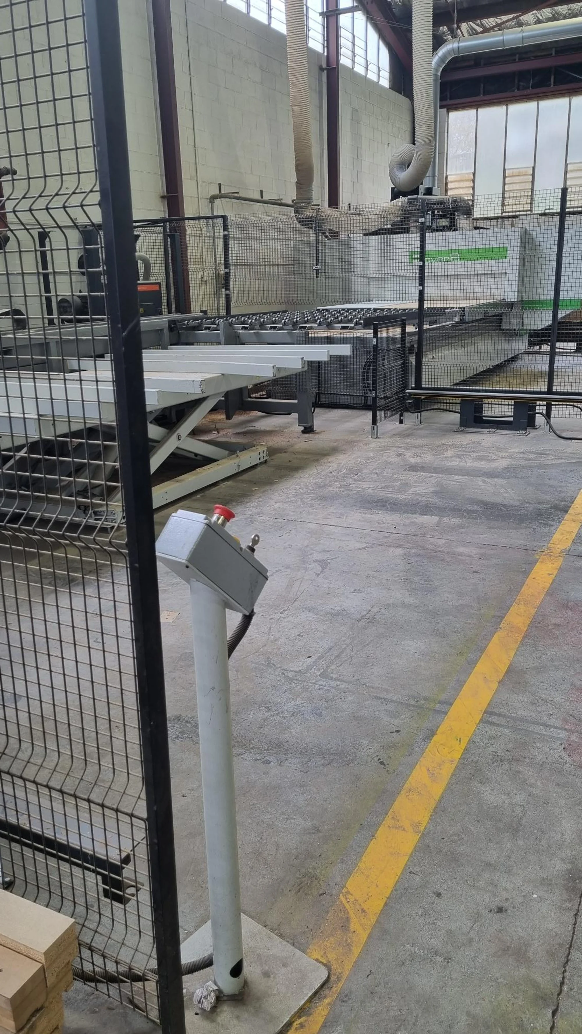 Industrial machine in a factory setting surrounded by safety fencing and a control panel.