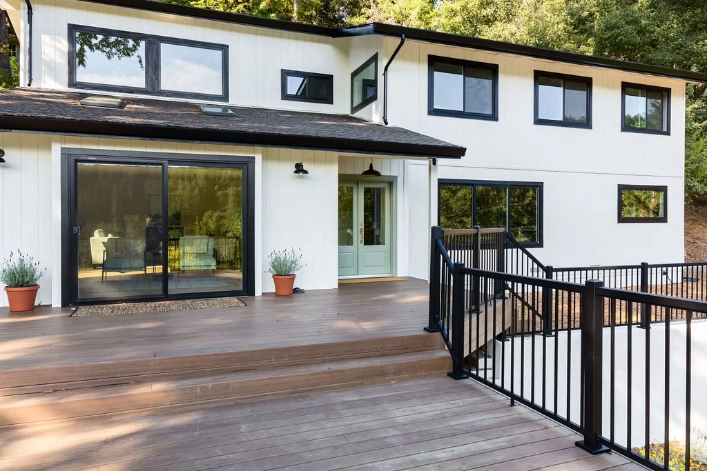 Remodeled two-story home with white vertical siding, black-framed windows and a wide deck with black metal railings, [near Felton, CA]