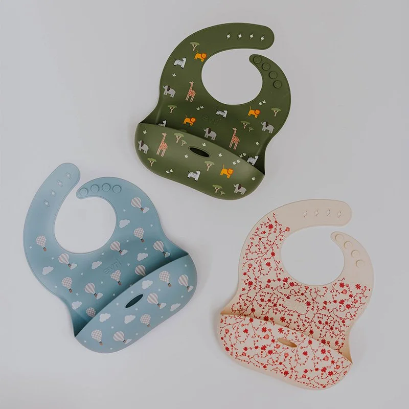 Three colorful disposable bibs with different patterns lying on a white surface.