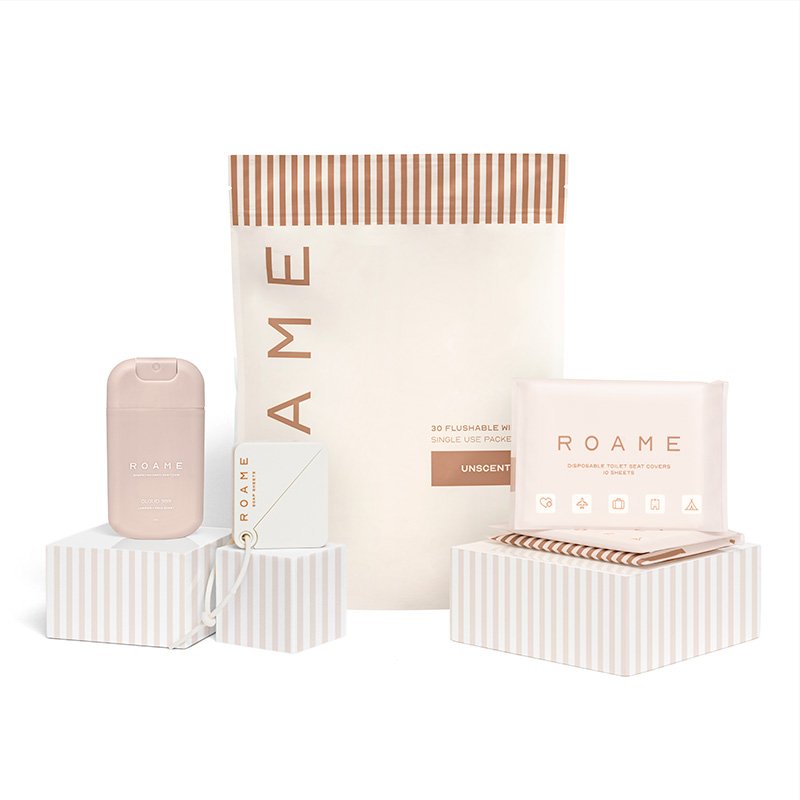 Collection of Roame personal care products including a flushable wipe pack, toilet covers, and a portable product container with a lid, all in light pink and beige packaging with striped accents.