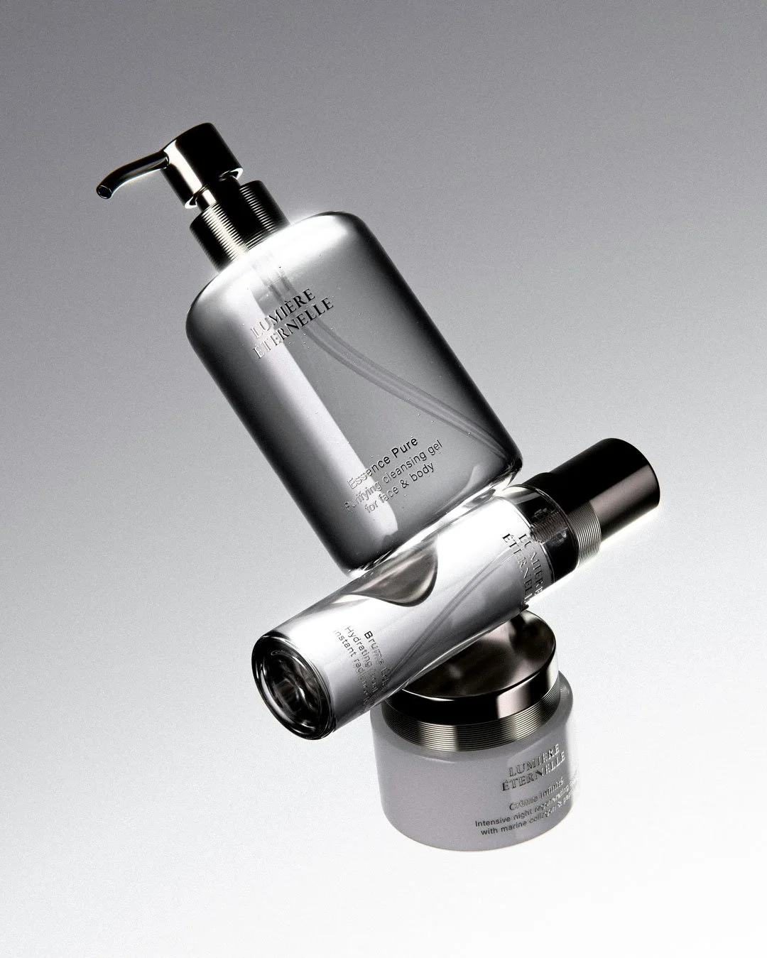 Set of skincare products, including a large silver bottle, a smaller clear bottle, and a small container, from the brand L'Occitane. The products are arranged on a gray background.