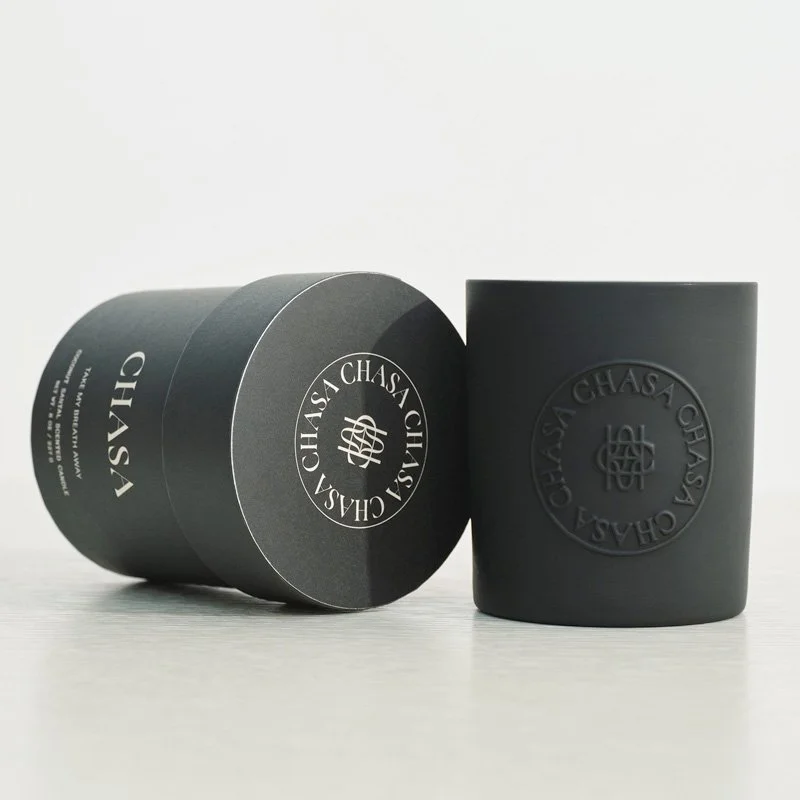 Black cylindrical container and matching black cup with round logo and text reading "CHASA CHASSA" on a light surface against a white background.