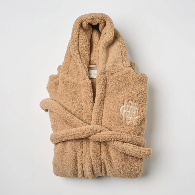 Beige sherpa bathrobe with a tie belt and embroidered logo on the chest, hanging against a white background.