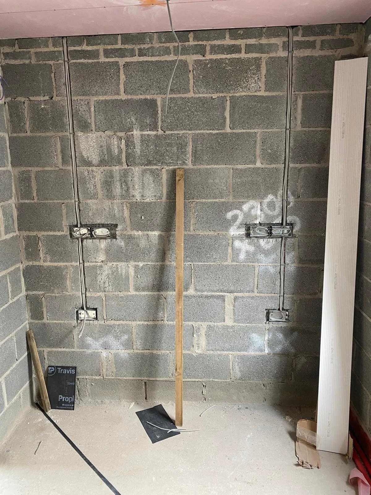 Interior wall under construction with electrical wiring and outlets installed, wooden and metal tools, and construction materials on the floor.
