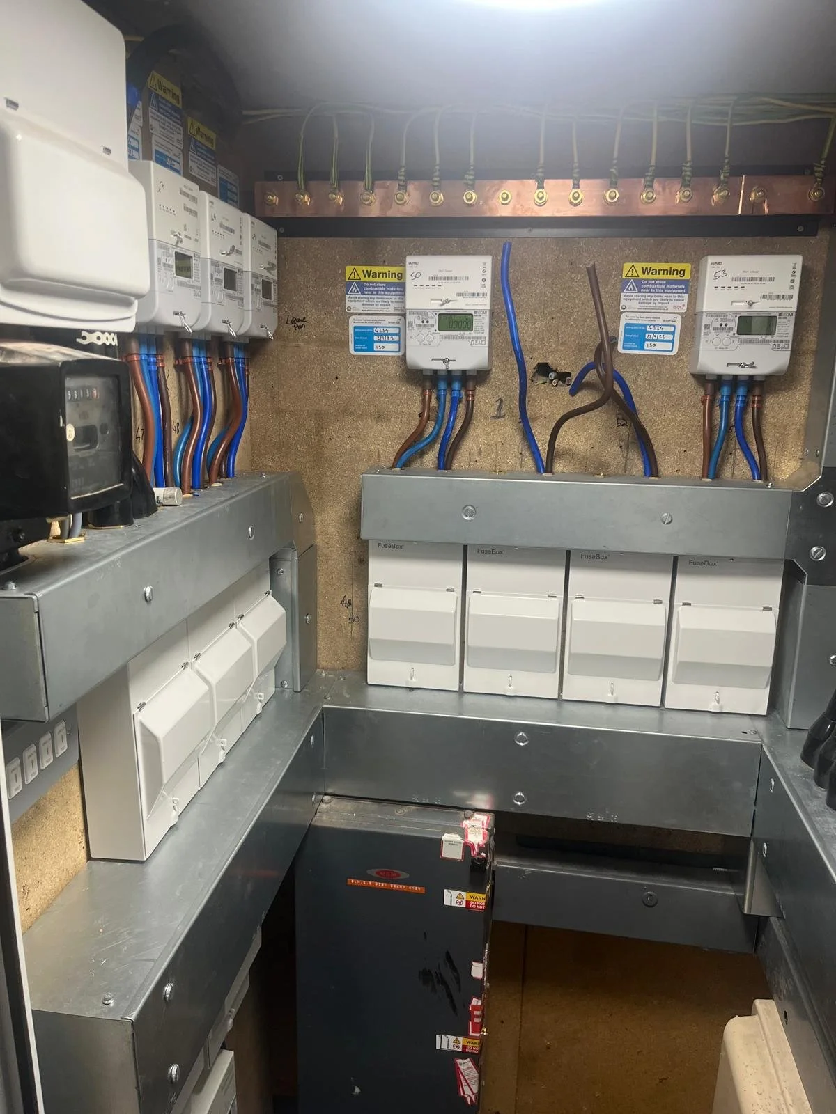 Electrical panel with circuit breakers, meters, and wiring in a utility room or control closet.