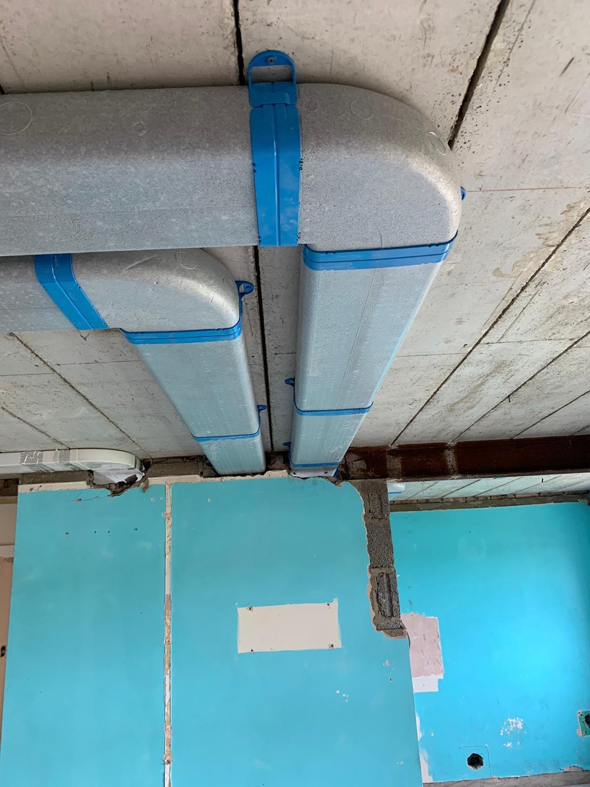 Construction site ceiling with grey insulation panels and blue electrical conduit piping installed.
