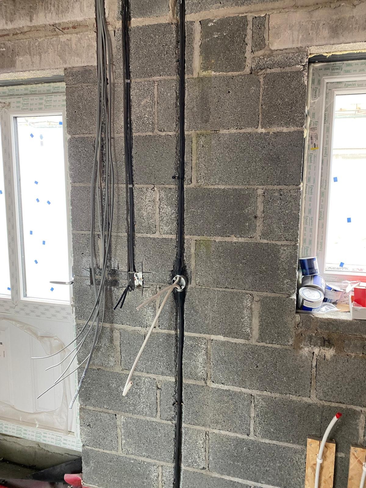 Interior of a building under construction or renovation, with exposed concrete block walls, wiring, and pipes.