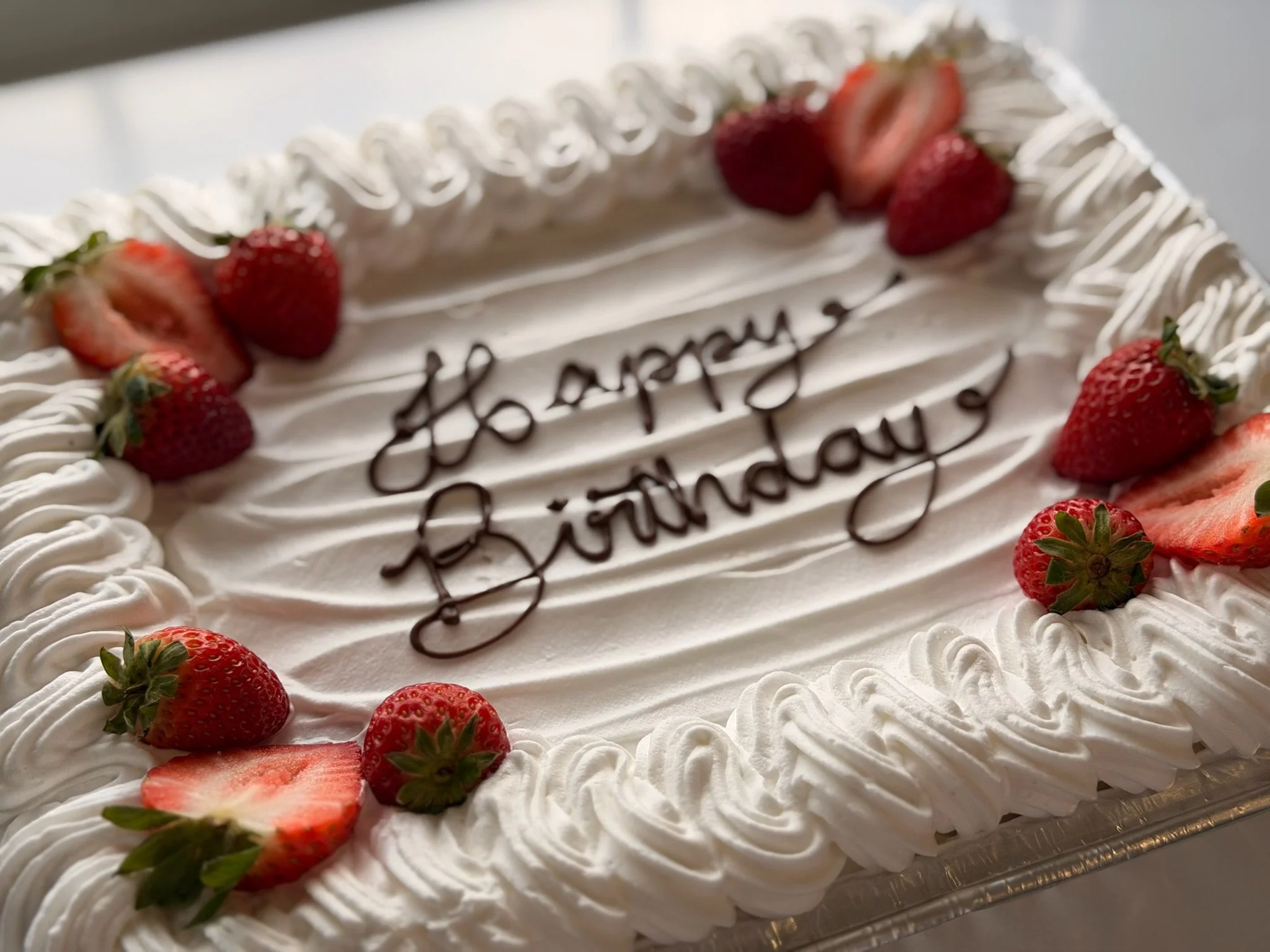 White birthday cake decorated with strawberries and a chocolate message that says "Happy Birthday."