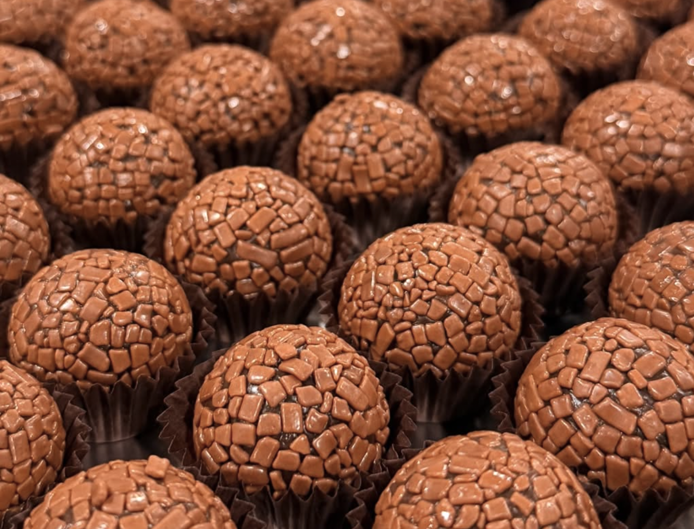 A close-up of numerous chocolate truffles covered with small chocolate sprinkles, arranged in a grid pattern.
