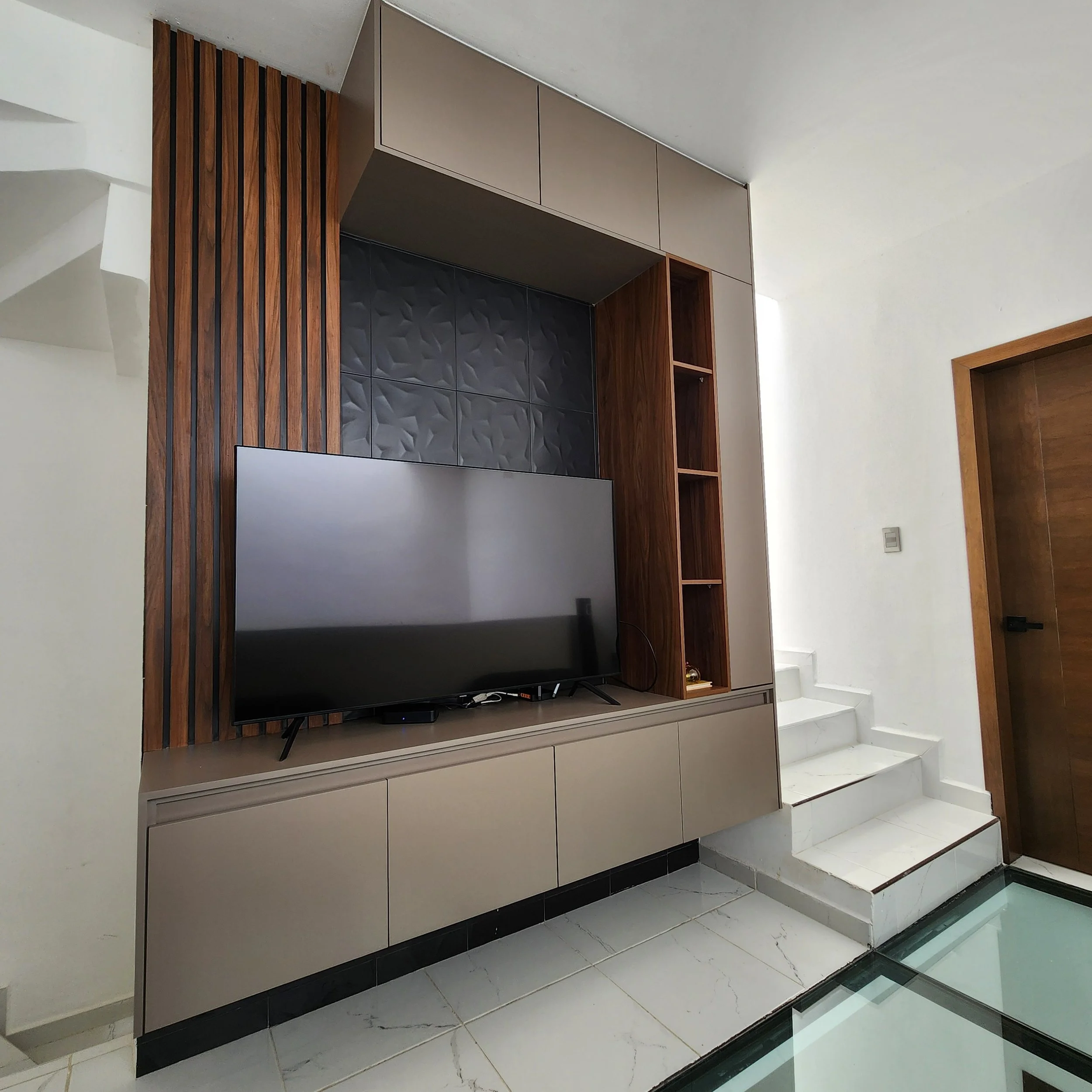 Panel de pared con acabado en color gris y armario abierto de madera, en un bonito diseño interior con suelo de mármol blanco con vetas grises y baldosas negras en el borde, en una zona de escaleras.
